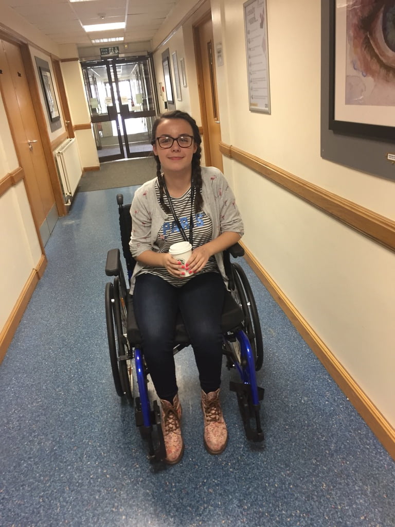 Teenage in a wheelchair in a corridor holding a coffee