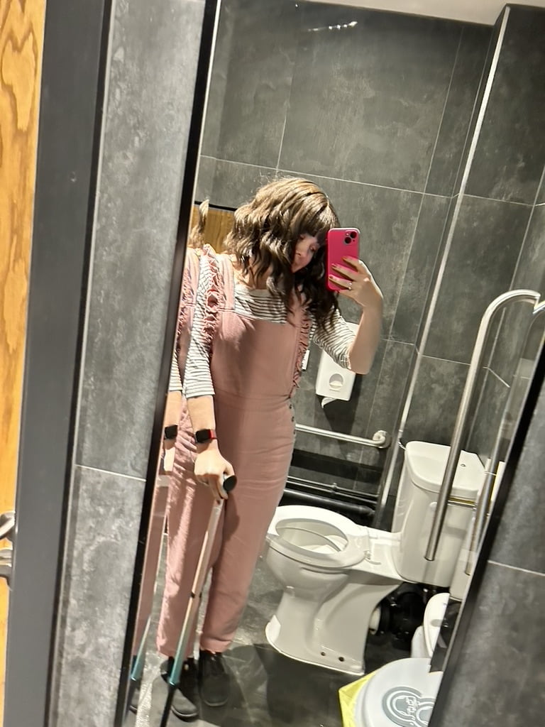 Woman in the toilet wearing pink dungerees and using a walking stick