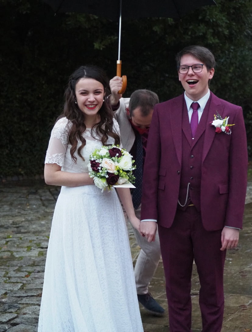 Newly married couple stood under an umbrella in the rain