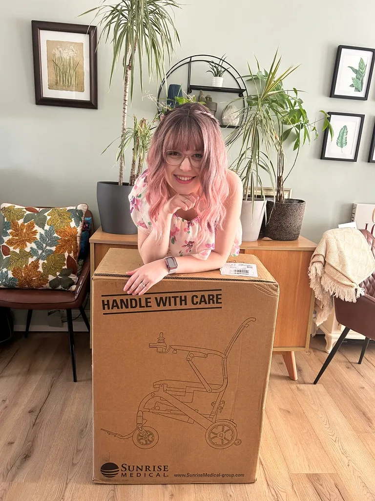 Lady with pink hair posting with Q50R wheelchair box