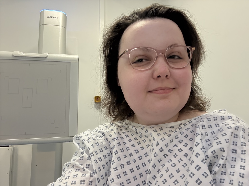 Early morning X-ray at 3am. Imali, with her natural, thin hair in a bob sitting near a machine wearing a hospital gown. 