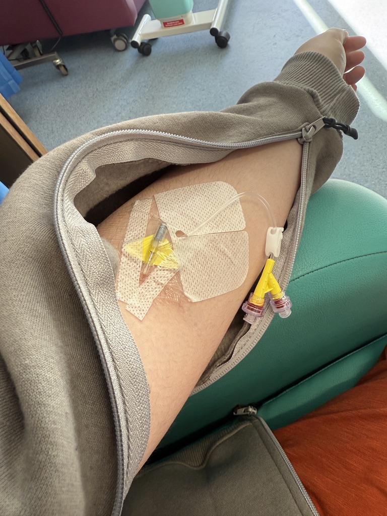 An arm, with an IV cannula inserted wearing an IV access hoodie top.