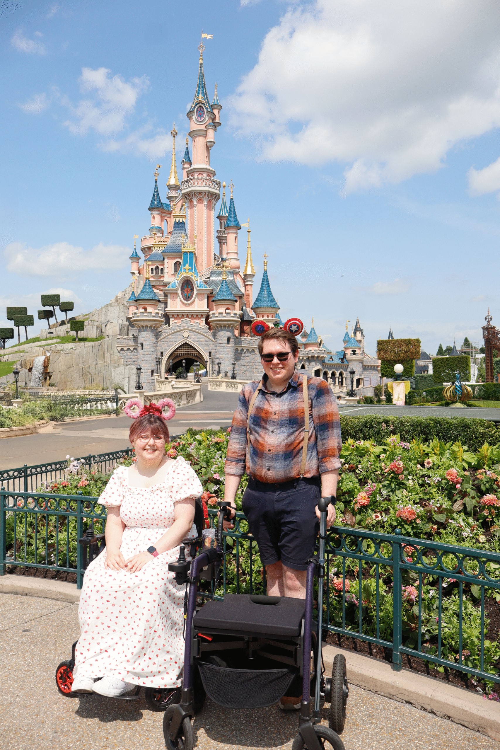 Imali and Cam, a white female and make, standing with two mobility aids in front of the castle at Disneyland Paris.