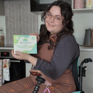 White woman with brown hair, sitting in a wheelchair wearing dungerees